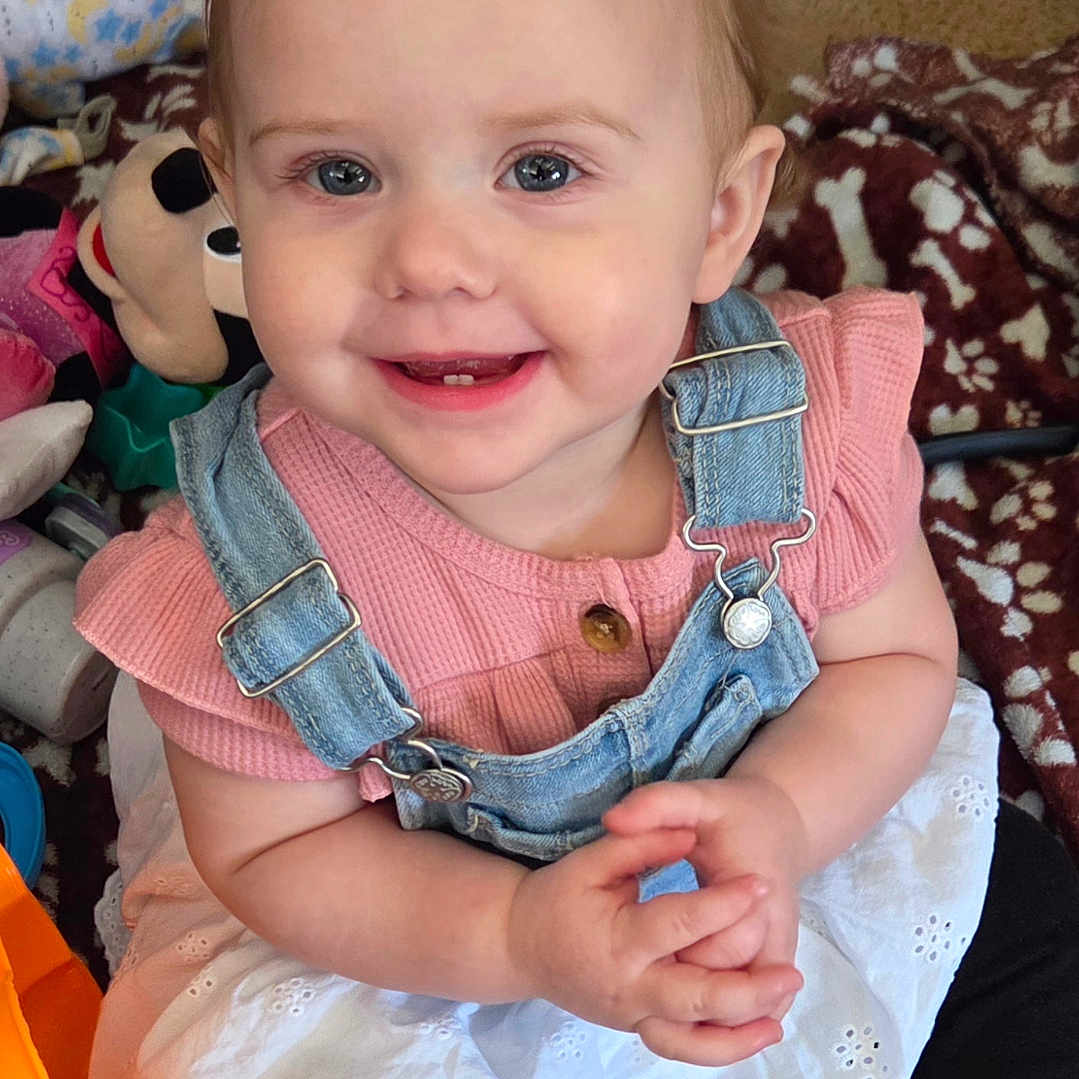 Mylah joined the competition — help win amazing prizes! baby, blanket, carpet, child, denim_overalls, eyes, face, hands, indoors, pink_shirt, playtime, plush_toy, ponytail, portrait, sitting, smiling, teeth, toddler, toys, white_skirt