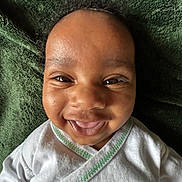 Jaceon is registered to the contest to win money with this photo: baby, infant, child, smiling, happy, portrait, face, eyes, close_up, indoor, blanket, green_blanket, white_clothing, onesie, lying_down, cozy, adorable, head, photograph, joy