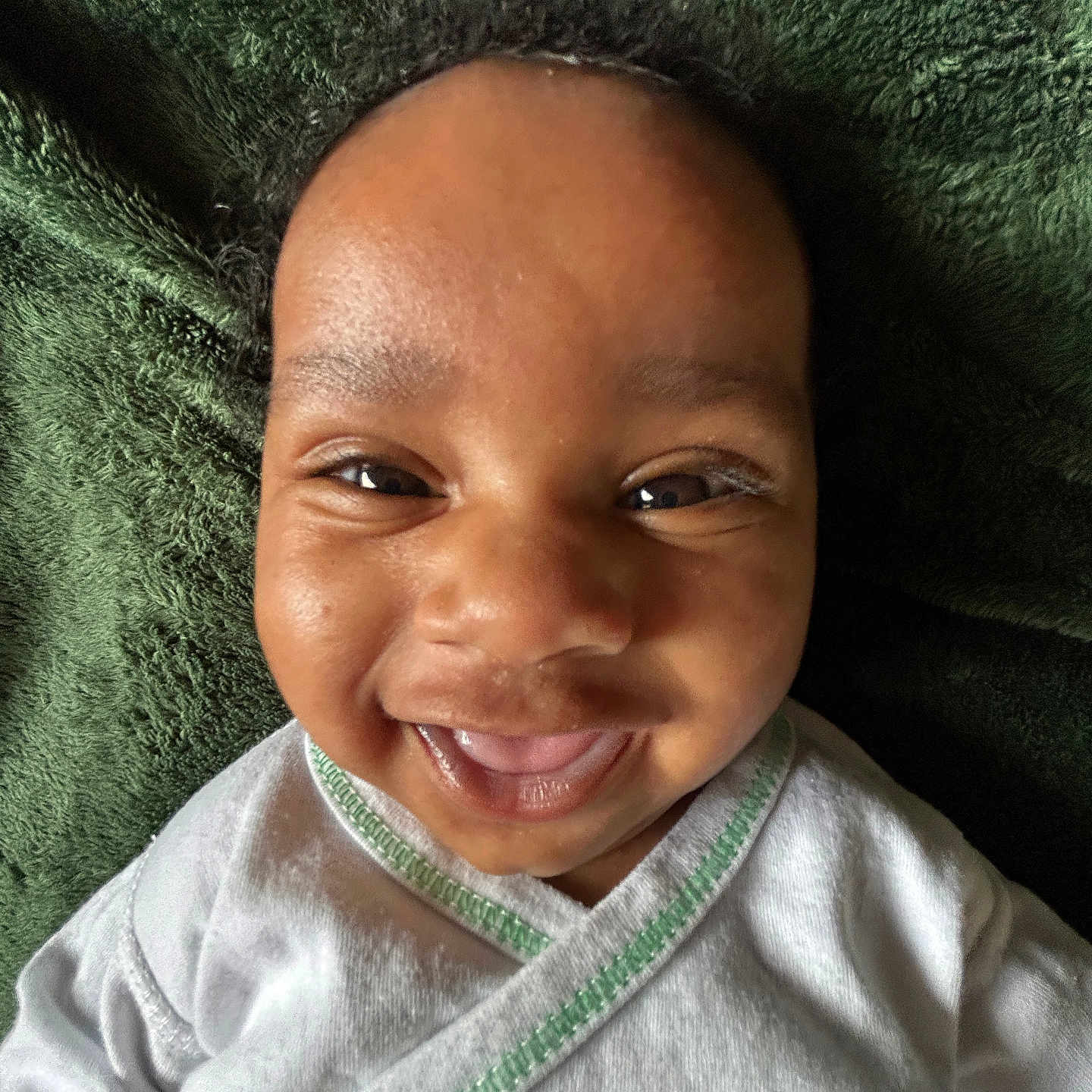 Jaceon is registered to the contest to win money with this photo: baby, infant, child, smiling, happy, portrait, face, eyes, close_up, indoor, blanket, green_blanket, white_clothing, onesie, lying_down, cozy, adorable, head, photograph, joy