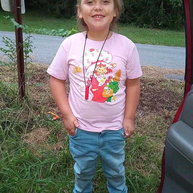 Rose is registered to the contest to win money with this photo: accessory, car, casual_clothing, child, daylight, footwear, grass, greenery, happy, jeans, nature, outdoor, person, portrait, road, smiling, sneakers, standing, trees, tshirt