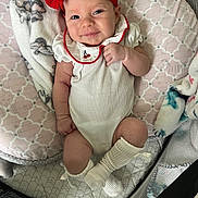 Charlee is registered to the contest to win money with this photo: baby, infant, smiling, red_bow, headband, white_outfit, blanket, cushion, soft_toys, lying_down, indoor, cute, child, happy, person, sock, playpen, patterned, cozy, portrait