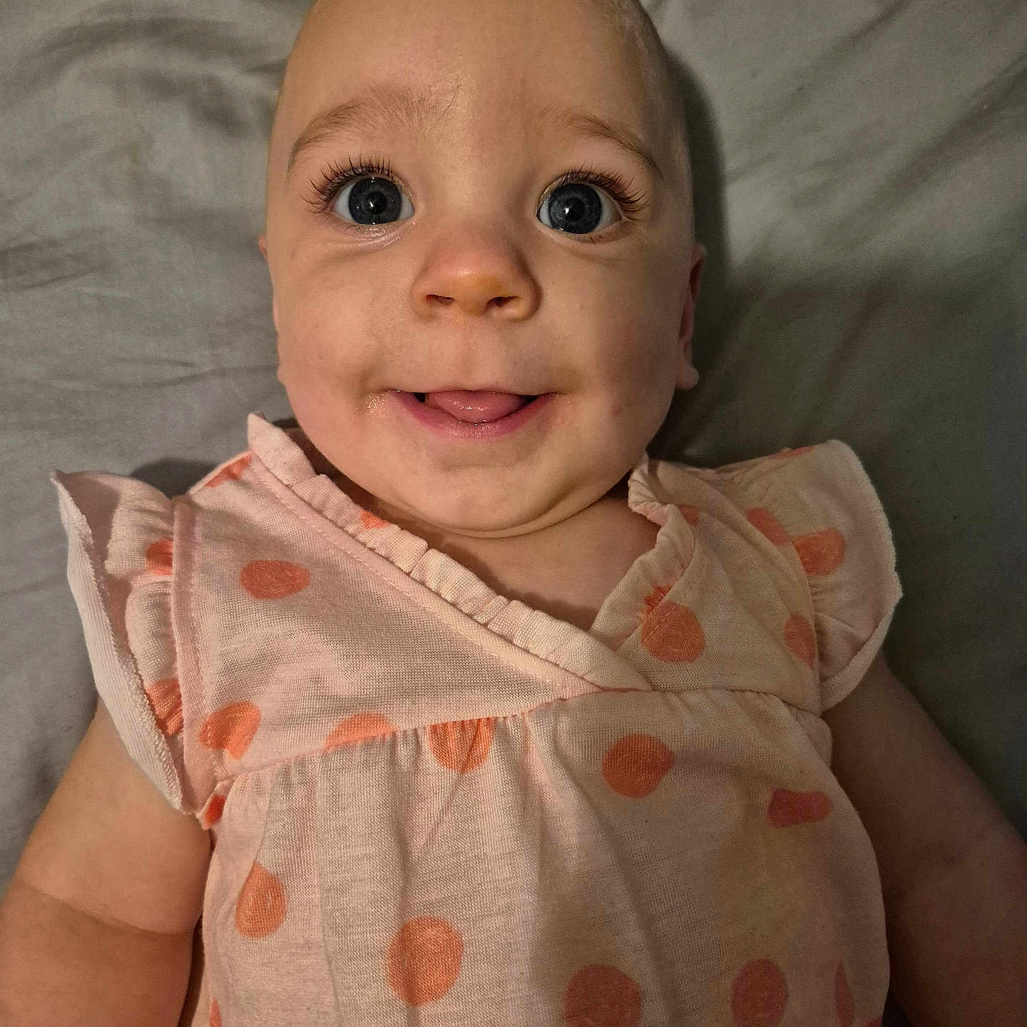 Sophia is registered to the contest to win money with this photo: baby, blue_eyes, child, close_up, cute, expression, eyes, face, happy, indoors, infant, long_eyelashes, lying_down, person, pink_dress, polka_dot, portrait, skin, smiling, soft_lighting