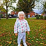 child, toddler, outdoor, autumn, park, leaves, grass, jacket, hat, smile, happy, shoes, pants, trees, residential_area, daylight, nature, playful, cute, seasonal