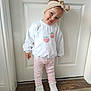 toddler, child, headband, white_sweater, strawberry_pattern, pink_pants, white_shoes, standing, indoors, door, wood_floor, carpet, cute, smiling, portrait, fashion, young_child, happy, casual_clothing, person