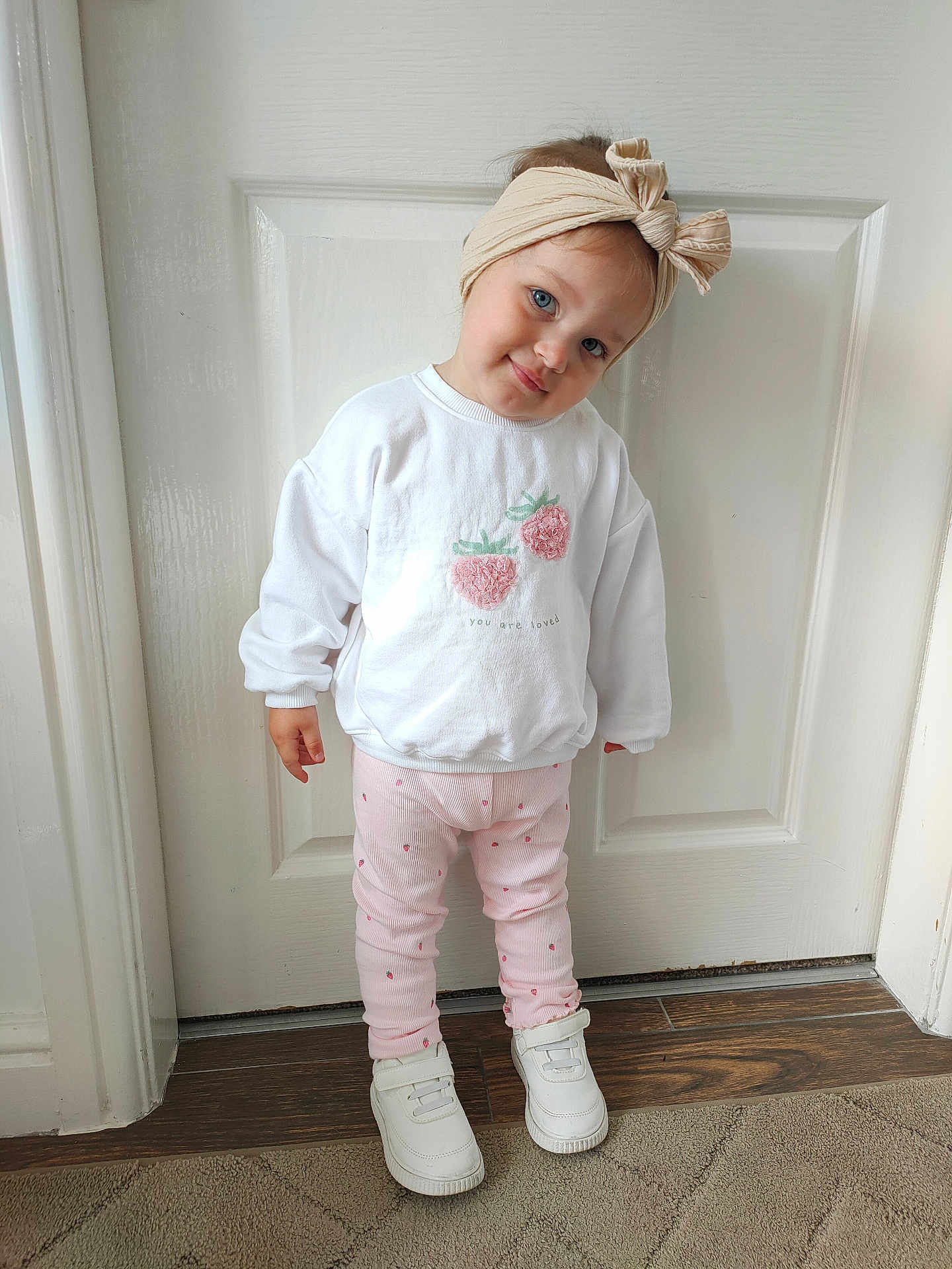 Lia joined the competition — help win amazing prizes! toddler, child, headband, white_sweater, strawberry_pattern, pink_pants, white_shoes, standing, indoors, door, wood_floor, carpet, cute, smiling, portrait, fashion, young_child, happy, casual_clothing, person