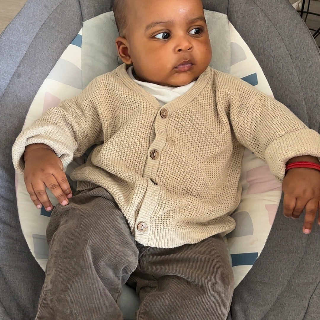 ïssah participe au concours pour gagner de l'argent avec cette photo : baby, baby_seat, casual_clothing, child, child_care, comfortable, cozy, cushion, cute, floor, hand, indoor, infant, looking_away, pants, person, ring, sock, sweater, wood_floor