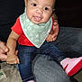 Nevaeh is registered to the contest to win money with this photo: baby, child, smiling, sitting, indoor, red_shirt, blue_jeans, pink_shoes, green_bib, person_holding, hands, happy, cute, infant, denim, footwear, casual_clothing, portrait, close_up, family