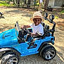 Kayden a rejoint le concours — aidez-le/la à gagner de superbes lots ! adult, blue, casual_clothing, child, daylight, dirt_ground, fun, happy, hat, nature, outdoor, park, person, play, recreation, smile, sunny, toy_car, trees, vehicle