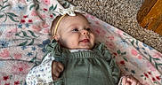 Ella joined the competition — help win amazing prizes! baby, infant, child, lying_down, smiling, face, headband, bow, green_outfit, floral_blanket, blanket, carpet, wood_floor, indoor, portrait, close_up, happy, hands, fashion, cute