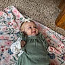 baby, infant, child, lying_down, smiling, face, headband, bow, green_outfit, floral_blanket, blanket, carpet, wood_floor, indoor, portrait, close_up, happy, hands, fashion, cute
