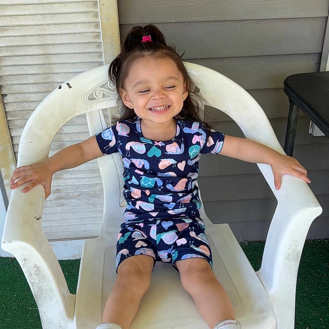 Liliana is registered to the contest to win money with this photo: chair, child, clothing, face, female, footwear, furniture, girl, grass, head, pants, person, photography, plant, portrait, sandal, shoe, shorts, sitting, sneaker