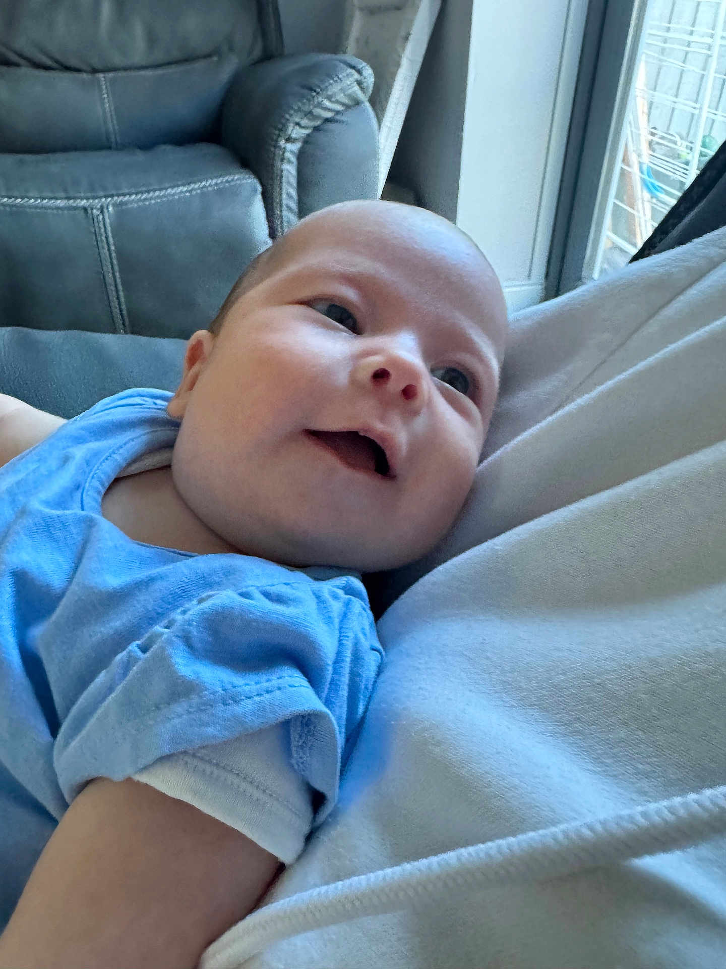Poppy is registered to the contest to win money with this photo: baby, child, blue_clothing, smile, face, infant, indoors, cozy, couch, upclose, portrait, happy, relaxed, soft_light, home, person, sleeve, skin, head, young