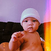 Idris is registered to the contest to win money with this photo: baby, infant, hat, diaper, person, skin, face, arm, hand, torso, couch, indoor, sitting, expression, curious, vintage_filter, light_leak, warm_tone, nostalgic, blurred_background