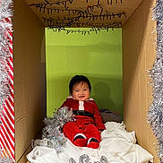 Tsoknyi a rejoint le concours — aidez-le/la à gagner de superbes lots ! baby, child, cardboard_box, christmas, holiday, tinsel, red_clothing, smile, festive, decoration, indoors, green_wall, white_cloth, sitting, cute, infant, person, celebration, happy, seasonal