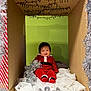 baby, child, cardboard_box, christmas, holiday, tinsel, red_clothing, smile, festive, decoration, indoors, green_wall, white_cloth, sitting, cute, infant, person, celebration, happy, seasonal