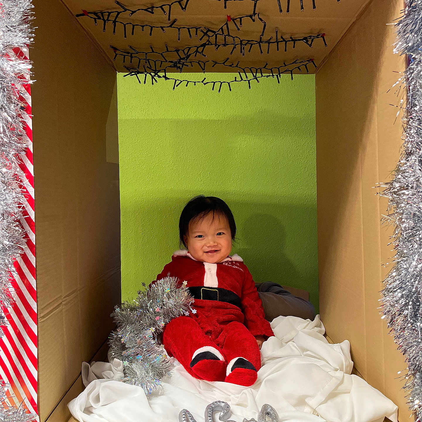 Tsoknyi a rejoint le concours — aidez-le/la à gagner de superbes lots ! baby, cardboard_box, celebration, child, christmas, cute, decoration, festive, green_wall, happy, holiday, indoors, infant, person, red_clothing, seasonal, sitting, smile, tinsel, white_cloth