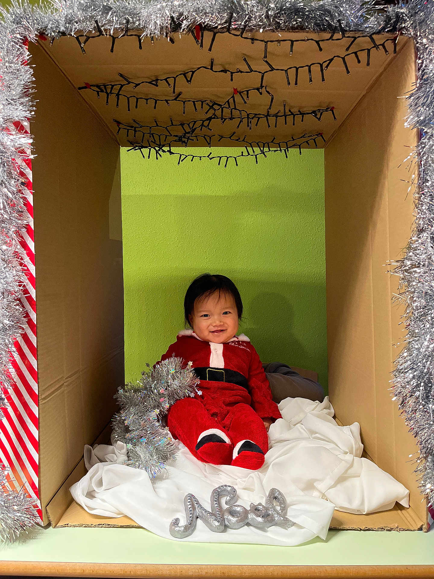 Tsoknyi a rejoint le concours — aidez-le/la à gagner de superbes lots ! baby, child, cardboard_box, christmas, holiday, tinsel, red_clothing, smile, festive, decoration, indoors, green_wall, white_cloth, sitting, cute, infant, person, celebration, happy, seasonal