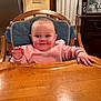 baby, child, high_chair, pink_sweatshirt, nike, wooden_chair, cushion, smiling, happy, indoor, kitchen, table, hand, face, person, photography, framed_photo, refrigerator, cabinet, light_switch