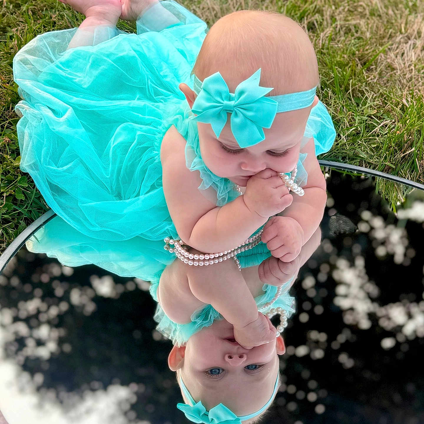 Ceaira is registered to the contest to win money with this photo: accessory, baby, barefoot, blue_dress, bow, child, curious, cute, dress, grass, headband, infant, mirror, nature, outdoor, pearls, playing, portrait, reflection, toddler