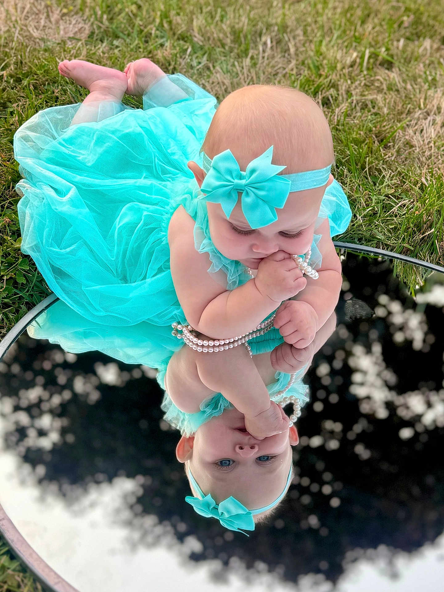 Ceaira is registered to the contest to win money with this photo: baby, child, toddler, dress, headband, bow, pearls, mirror, reflection, grass, outdoor, cute, infant, blue_dress, accessory, portrait, playing, barefoot, nature, curious