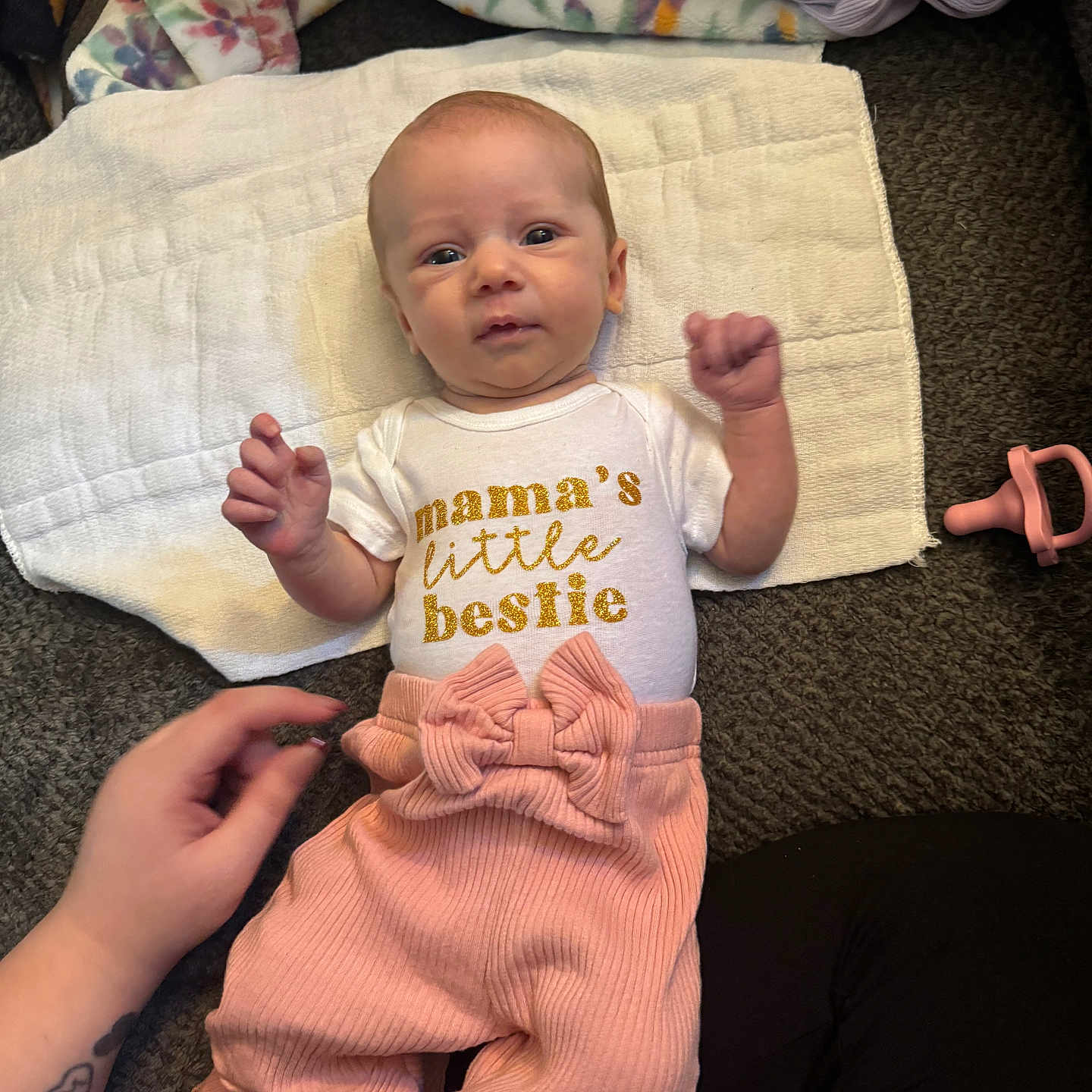 Kaisyn is registered to the contest to win money with this photo: baby, infant, towel, carpet, pacifier, pink_pants, white_shirt, text_on_clothing, hand, tattoo, floor, person, cute, child, lying_down, indoor, apparel, expression, newborn, accessory