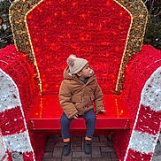 Kaylan participe au concours pour gagner de l'argent avec cette photo : child, toddler, winter_clothing, pacifier, red_throne, holiday_decorations, lights, snowflakes, outdoor, pavement, hat, jacket, boots, festive, christmas, seat, tree, decor, cute, cold_weather