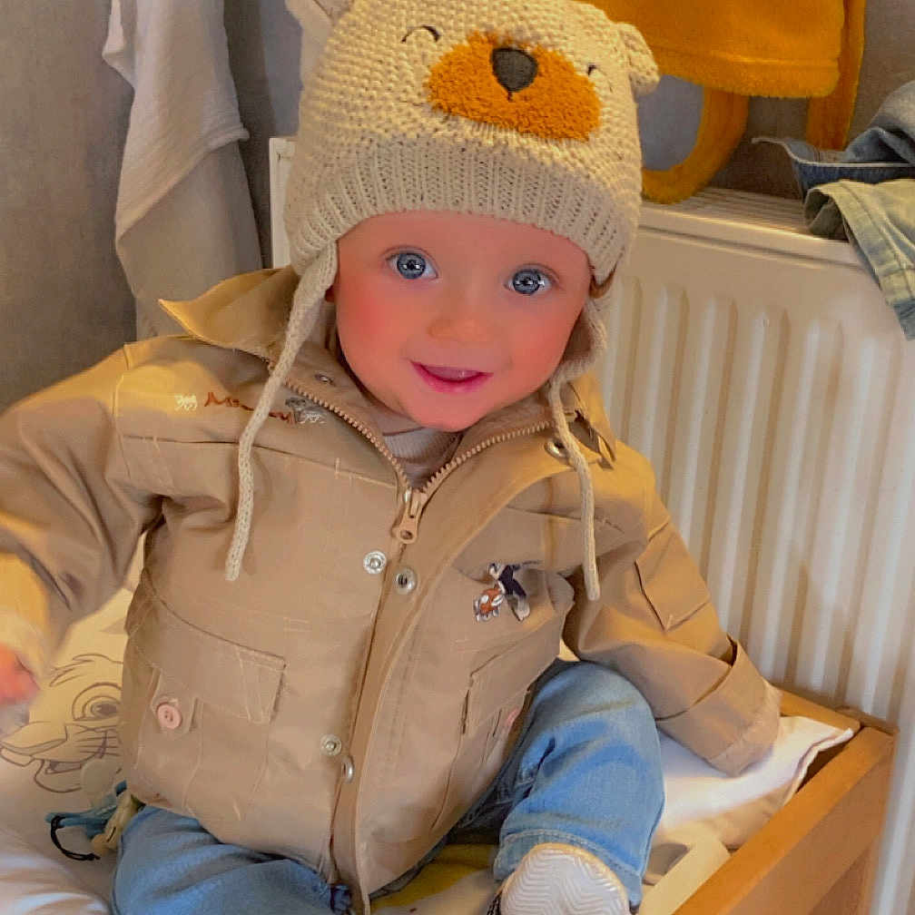 Eden participe au concours pour gagner de l'argent avec cette photo : animal_print, baby, beige_jacket, blanket, blue_jeans, changing_table, child, clothing, cute, face, hat, home, indoor, jacket, knitted_hat, person, shoes, smiling, toddler, warm_lighting