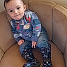 toddler, child, indoor, cushioned_chair, beige, long_sleeve_shirt, sea_creatures, denim_jeans, rain_boots, patterned_boots, smile, dimples, cute, casual_clothing, portrait, young_child, seated, comfortable, home, furniture