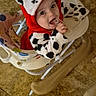 baby, child, hoodie, dalmatian_pattern, walker, floor, tile, indoor, cute, smiling, clothing, person, young_child, chewing, colorful, seat, playful, happy, face, hand