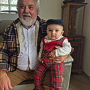 Elyas a rejoint le concours — aidez-le/la à gagner de superbes lots ! elderly_man, baby, plaid_clothing, indoor, living_room, furniture, window, glass_blocks, portrait, seated, shoe, hat, beard, smile, wooden_floor, cabinet, decor, casual_clothing, family, generations
