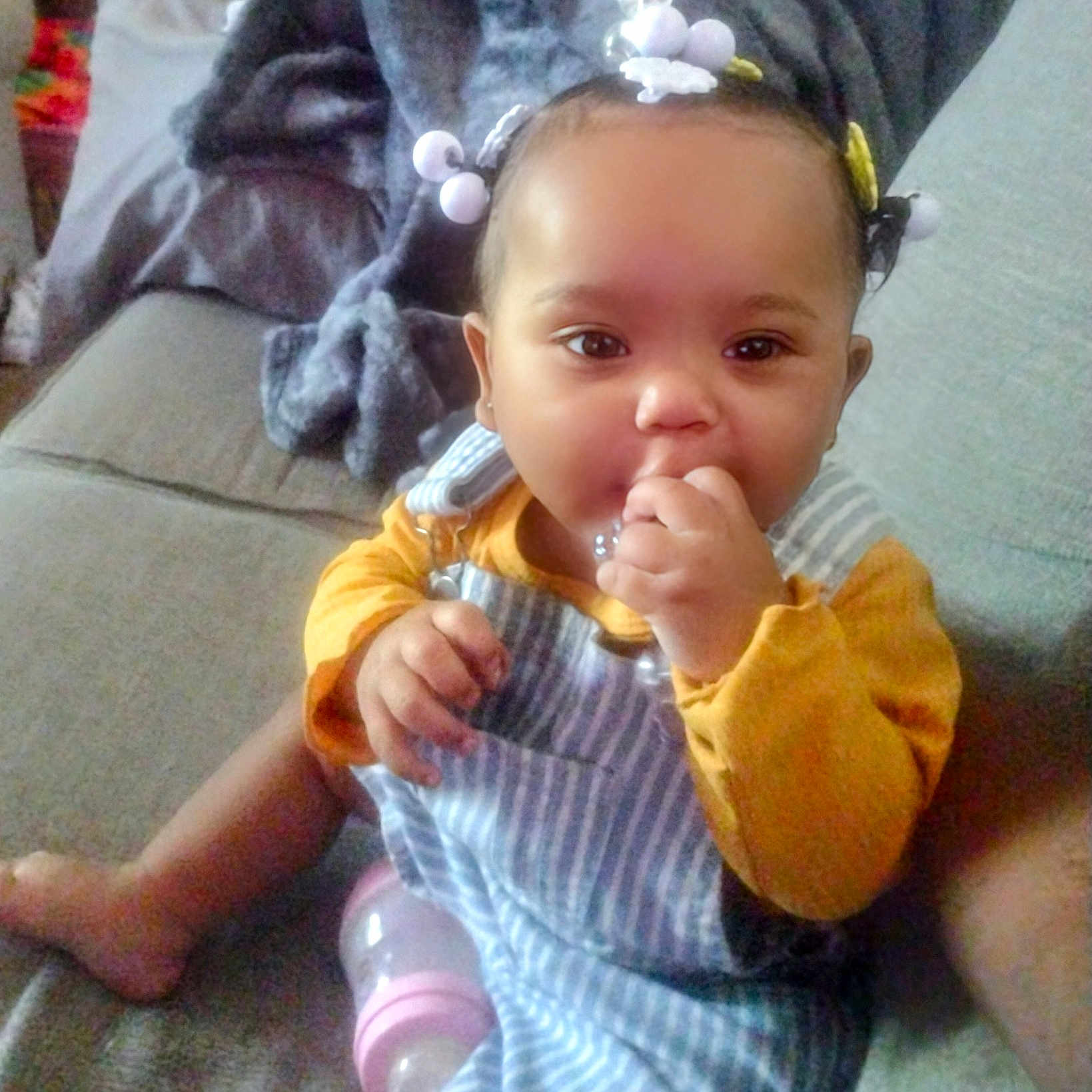 Tymeleanne is registered to the contest to win money with this photo: baby, blanket, bottle, child, couch, cozy, cute, face, foot, furniture, hair_beads, hand, home, indoor, infant, person, portrait, sitting, striped_overall, yellow_shirt