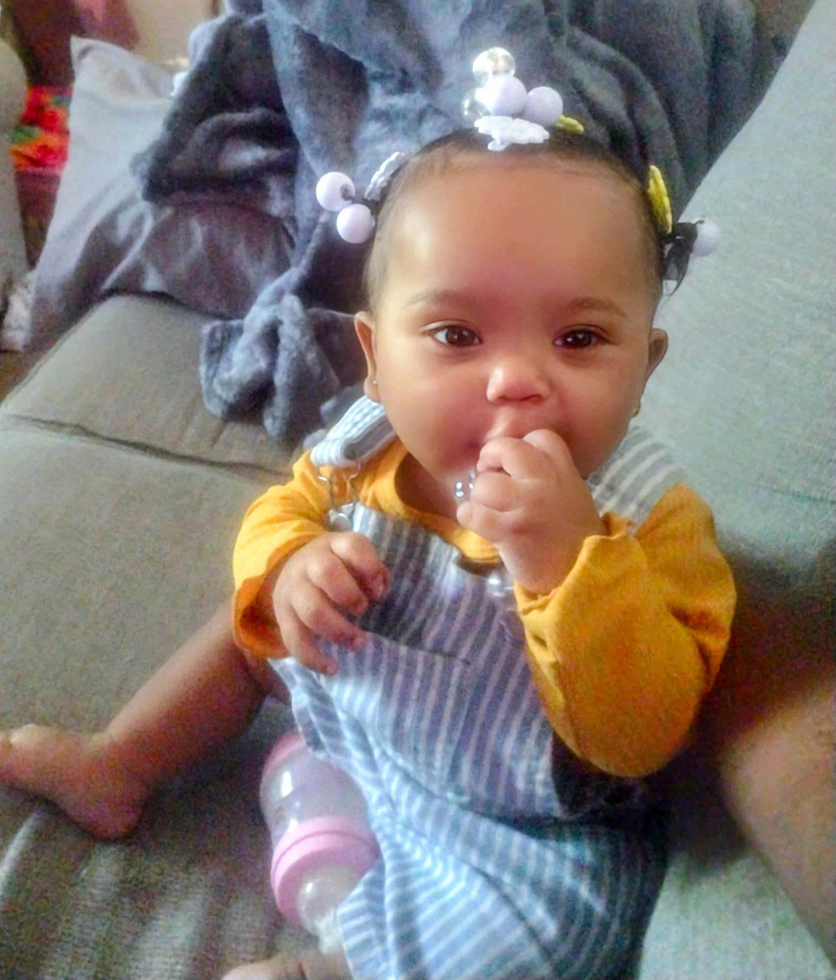 Tymeleanne is registered to the contest to win money with this photo: baby, child, couch, blanket, bottle, hair_beads, striped_overall, yellow_shirt, indoor, person, infant, sitting, cute, face, hand, foot, furniture, home, cozy, portrait