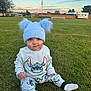 baby, child, grass, outdoor, blue_hat, pom_poms, sweater, pants, socks, field, sky, sunset, cute, sitting, young_child, stitch_character, clothing, nature, portrait, daylight