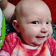 Macie is registered to the contest to win money with this photo: baby, infant, face, smile, cheeky, tie_dye, shirt, drool, close_up, person, child, skin, head, expression, cute, indoors, bright_eyes, cheek, colorful_clothing, playful