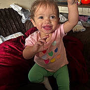 Avah joined the competition — help win amazing prizes! toddler, child, smiling, happy, indoor, cozy, blanket, pink_shirt, green_pants, heart_pattern, hair, face, person, couch, home, clothing, socks, furniture, playful, cute
