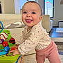 baby, child, toy, activity_center, indoor, living_room, smiling, happy, clothing, long_sleeve, pants, barefoot, floor_rug, furniture, window, daylight, person, cute, playful, home