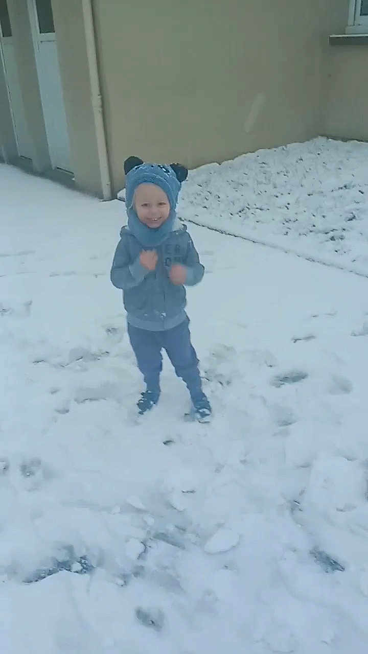 Ayden participe au concours pour gagner de l'argent avec cette photo : child, snow, winter, hat, blue_clothing, smiling, outdoor, building, footprints, cold, snowy_ground, coat, pants, shoes, wall, playful, happy, kid, scarf, headwear