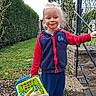 Ayden participe au concours pour gagner de l'argent avec cette photo : basket, candy, casual_clothing, child, daylight, grass, greenery, happy, holding, jacket, metal_railing, nature, outdoor, pants, person, playful, smile, stone_wall, toy, young_child