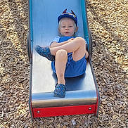 Ayden a rejoint le concours — aidez-le/la à gagner de superbes lots ! blue_clothing, cap, casual, child, crocs, crossed_legs, daylight, footwear, fun, kid, metal, outdoor, person, play, playground, recreation, slide, summer, wood_chips, young