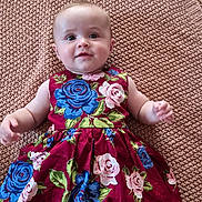 Louise a rejoint le concours — aidez-le/la à gagner de superbes lots ! baby, child, infant, dress, floral_pattern, knitted_blanket, smile, portrait, cute, lying_down, blue_eyes, pink_roses, blue_roses, colorful_clothing, soft_texture, skin, happy, young_child, indoors, close_up