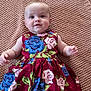 baby, child, infant, dress, floral_pattern, knitted_blanket, smile, portrait, cute, lying_down, blue_eyes, pink_roses, blue_roses, colorful_clothing, soft_texture, skin, happy, young_child, indoors, close_up