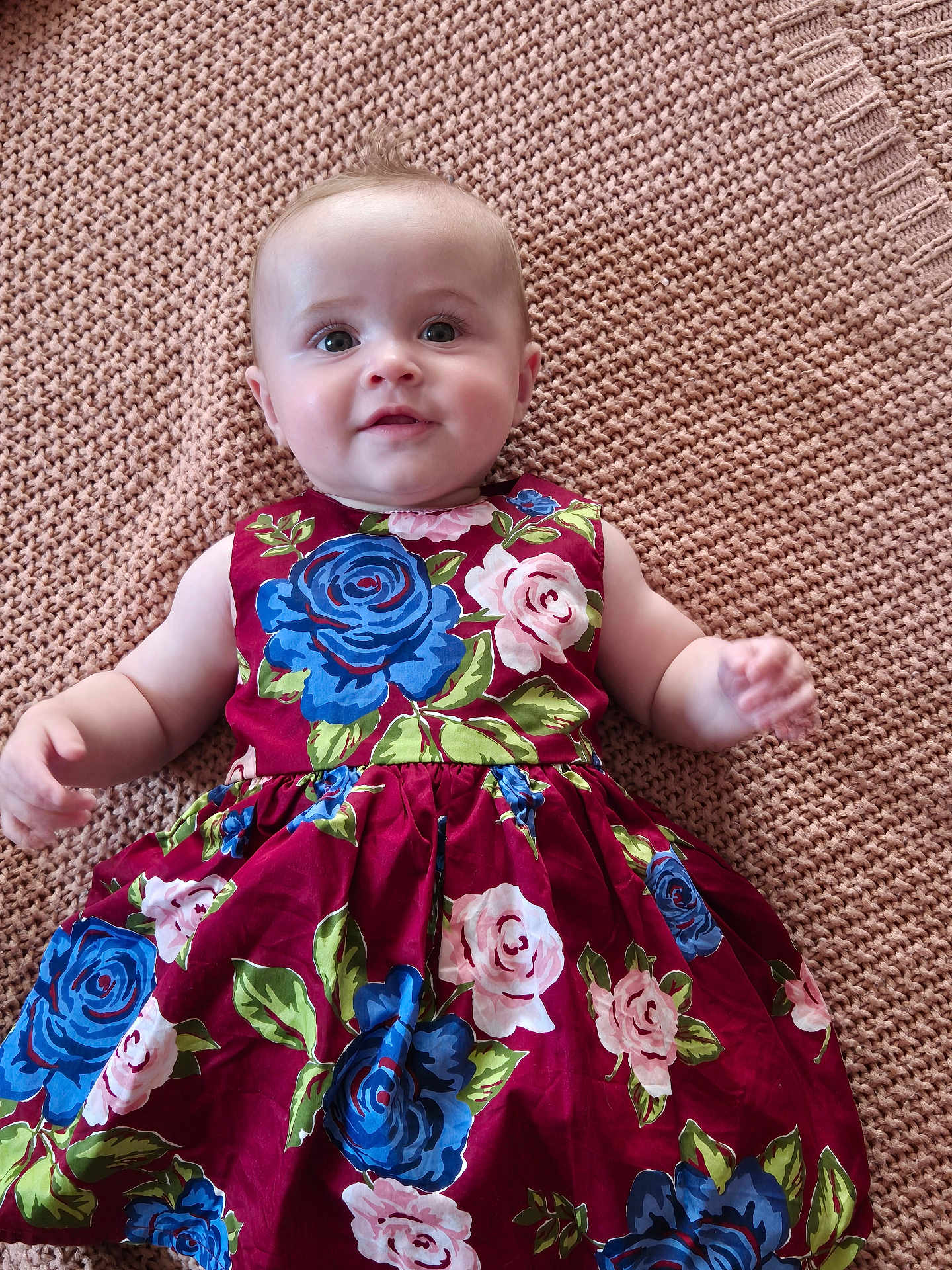 Louise a rejoint le concours — aidez-le/la à gagner de superbes lots ! baby, child, infant, dress, floral_pattern, knitted_blanket, smile, portrait, cute, lying_down, blue_eyes, pink_roses, blue_roses, colorful_clothing, soft_texture, skin, happy, young_child, indoors, close_up