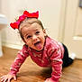 Emberlee is registered to the contest to win money with this photo: toddler, child, red_bow, pink_sweater, crawling, tongue_out, happy, playful, indoor, wooden_floor, cute, person, smiling, young_child, fun, casual_clothing, headwear, expression, portrait, home