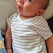 Ethan a rejoint le concours — aidez-le/la à gagner de superbes lots ! baby, infant, child, onesie, striped_clothing, tongue_out, face, skin, hand, blanket, soft_texture, cushion, indoor, cute, expression, portrait, newborn, person, young_child, resting