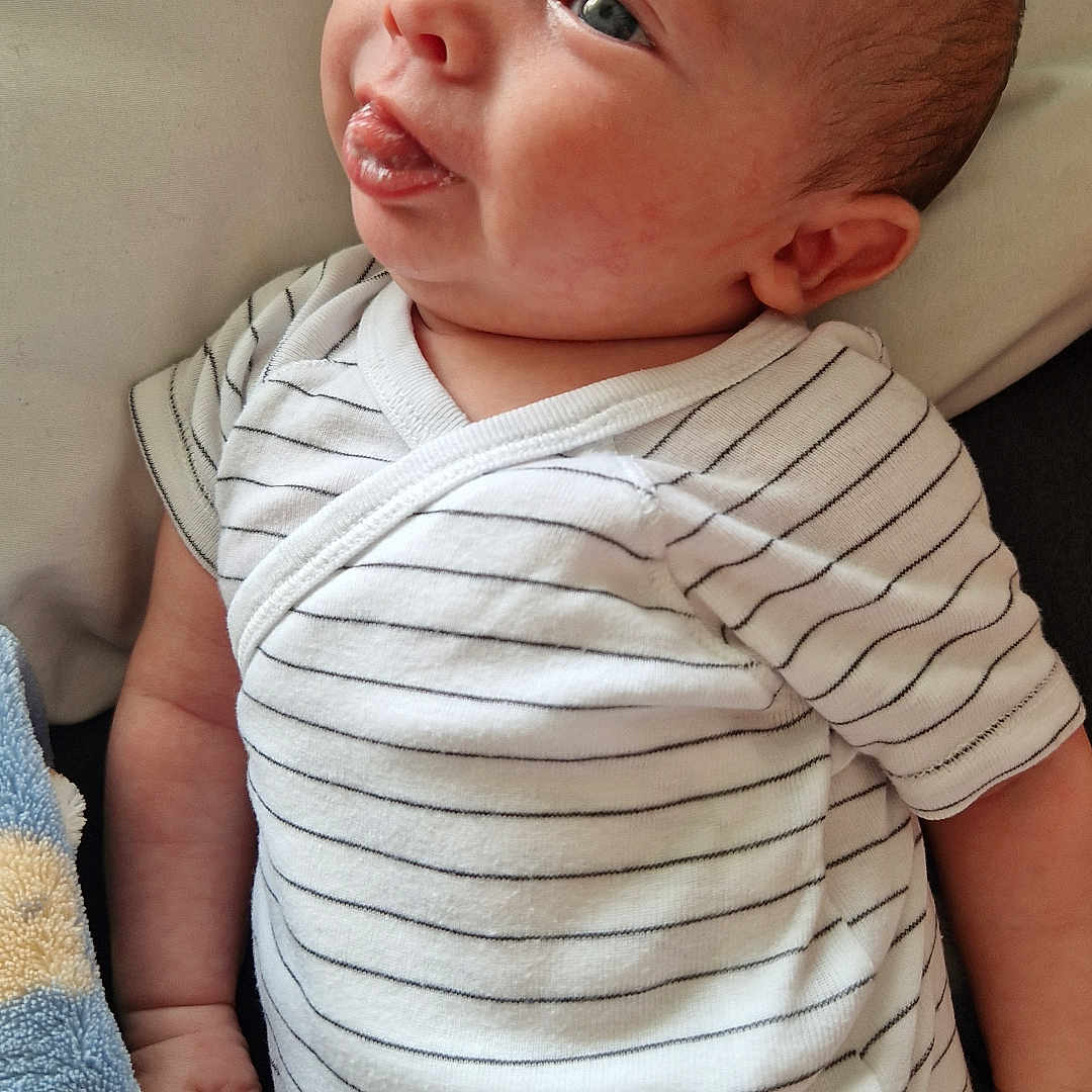 Ethan a rejoint le concours — aidez-le/la à gagner de superbes lots ! baby, blanket, child, cushion, cute, expression, face, hand, indoor, infant, newborn, onesie, person, portrait, resting, skin, soft_texture, striped_clothing, tongue_out, young_child