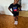 Victoria a rejoint le concours — aidez-le/la à gagner de superbes lots ! child, girl, smiling, glasses, black_tshirt, haitian_flag, shorts, sneakers, wooden_floor, refrigerator, magnets, indoor, standing, bracelet, earrings, confident_pose, person, happy, hair_beads, home