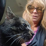 Stich is registered to the contest to win money with this photo: cat, tabby_cat, woman, glasses, long_hair, indoor, close_up, pet, animal, face, whiskers, person, portrait, casual_clothing, natural_light, seated, looking, feline, companion, cozy