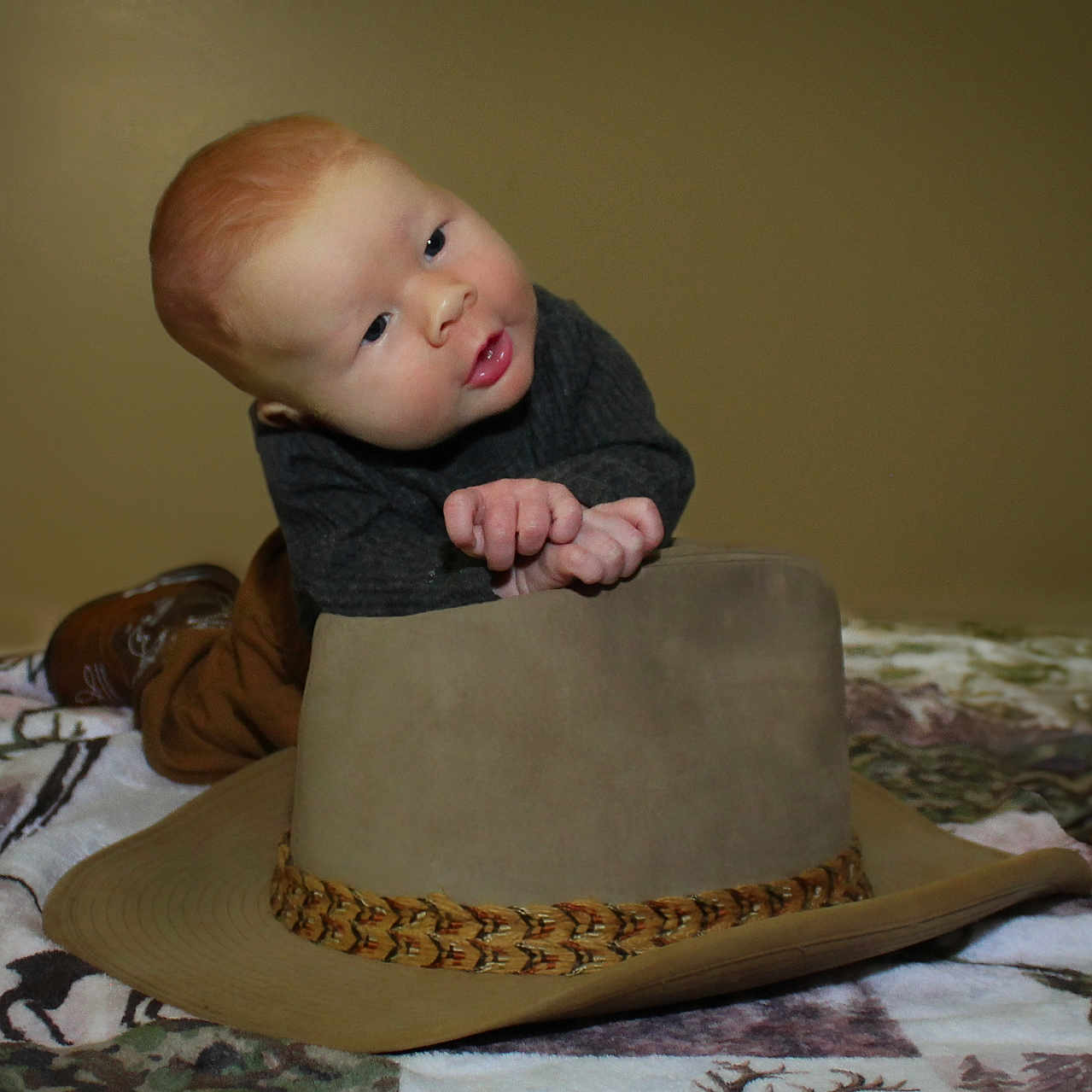 Luke joined the competition — help win amazing prizes! baby, baby_pose, blanket, child, clothing, cowboy_hat, curious, cute, face, ginger_hair, hands, hat, head, indoor, infant, neutral_background, patterned_blanket, portrait, resting, young