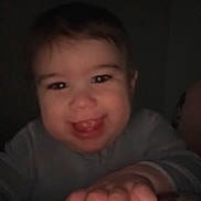 Keagan is registered to the contest to win money with this photo: baby, smiling, child, hand, face, portrait, dark_background, indoor, cute, clothing, infant, person, happy, young, skin, head, expression, human, baby_girl, closeup