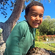 Ismael a rejoint le concours — aidez-le/la à gagner de superbes lots ! child, smiling, tree, outdoor, nature, green_sweater, sunlight, happy, boy, face, climbing, blue_sky, daylight, park, casual_clothing, grass, leaves, trunk, person, portrait